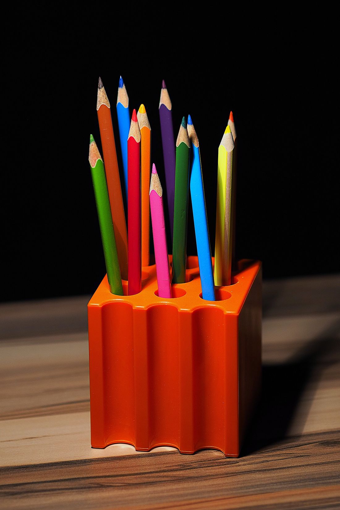 Portalápices naranja con lápices de colores sobre una mesa de madera
