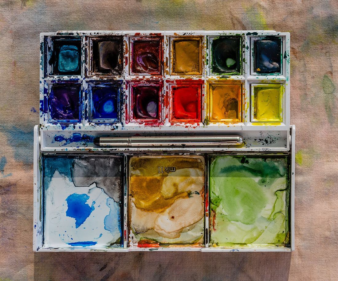 Caja de acuarelas en pastilla abierta, con colores usados y un pincel