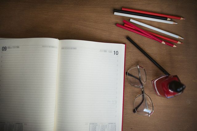 Agenda abierta en una semana en blanco, con lápices de colores y anteojos sobre un escritorio de madera